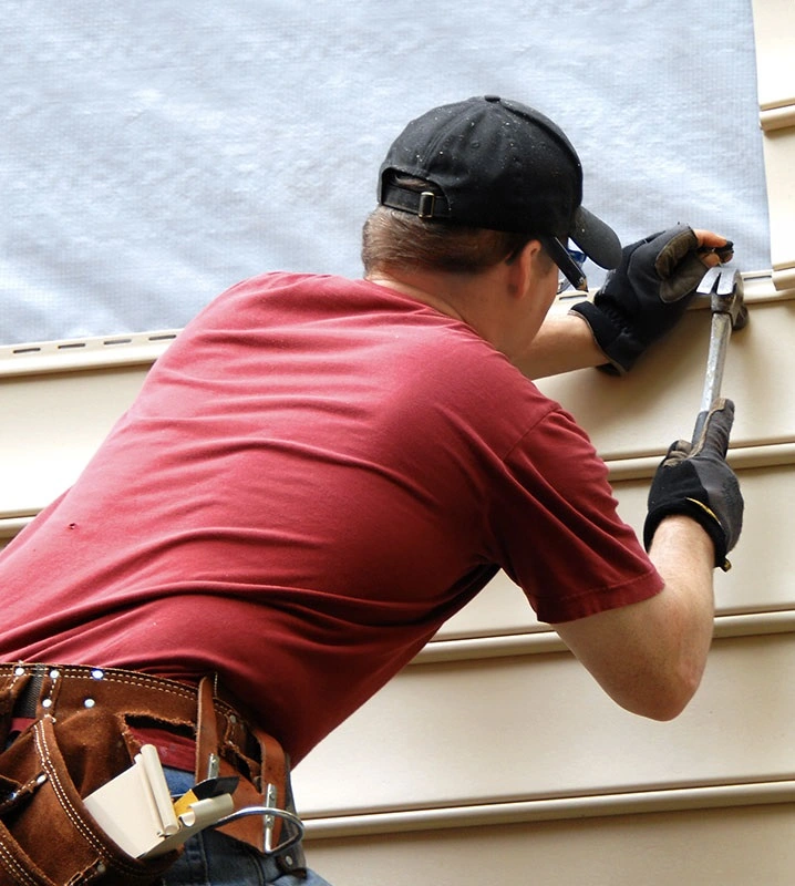 A man drilling shingles into a roof