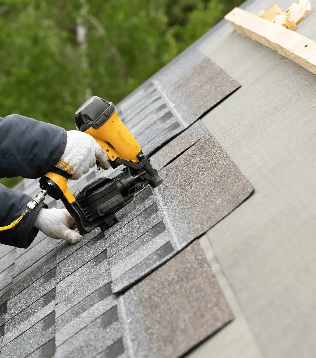 A man drilling shingles into a roof